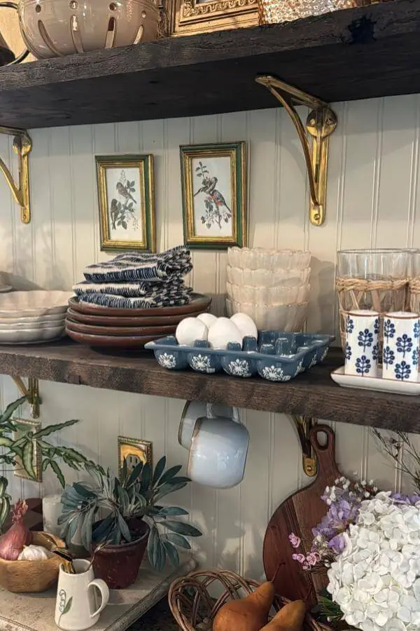 Rustic kitchen shelving with blue white ceramics from @ruefer.heartandhome. Vintage botanical prints complete the cozy display.