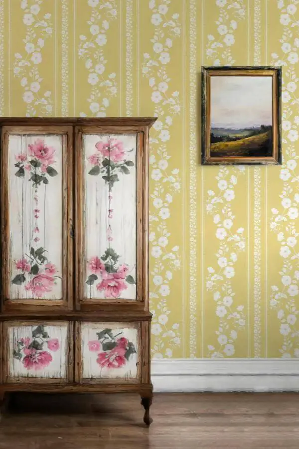 Vintage wooden cabinet with painted pink roses from @schatzibrown. Yellow floral wallpaper creates cozy cottage atmosphere.