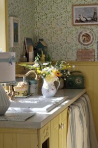 Cream kitchen cabinetry from @cooneynest. Vintage floral wallpaper and fresh flowers complete the cozy traditional styling.