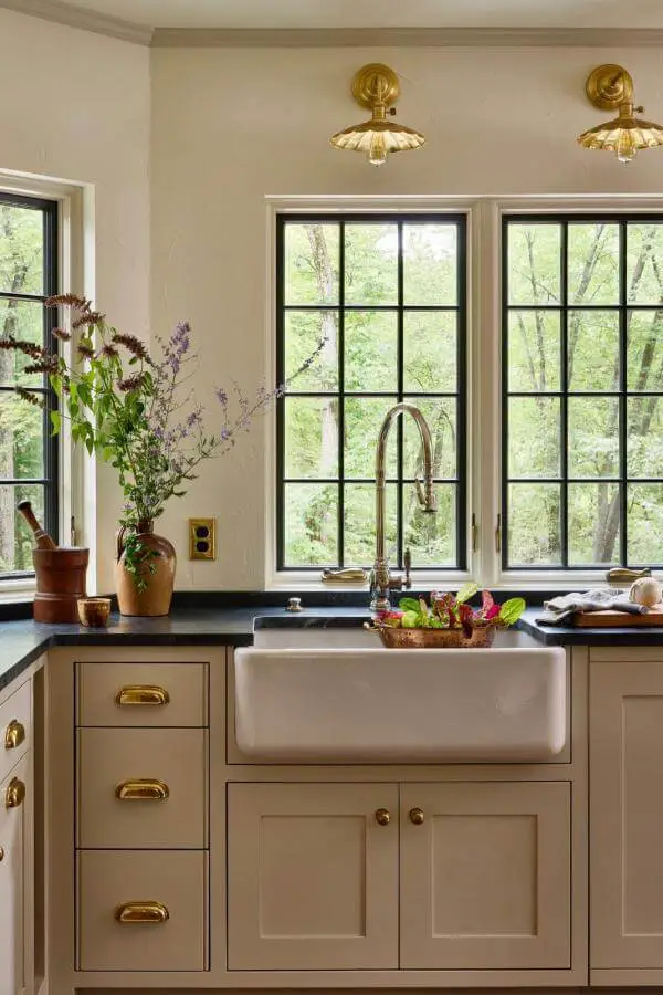 Sage green kitchen cabinets from @katierosenfeld. Features brass hardware and farmhouse sink with garden view windows.