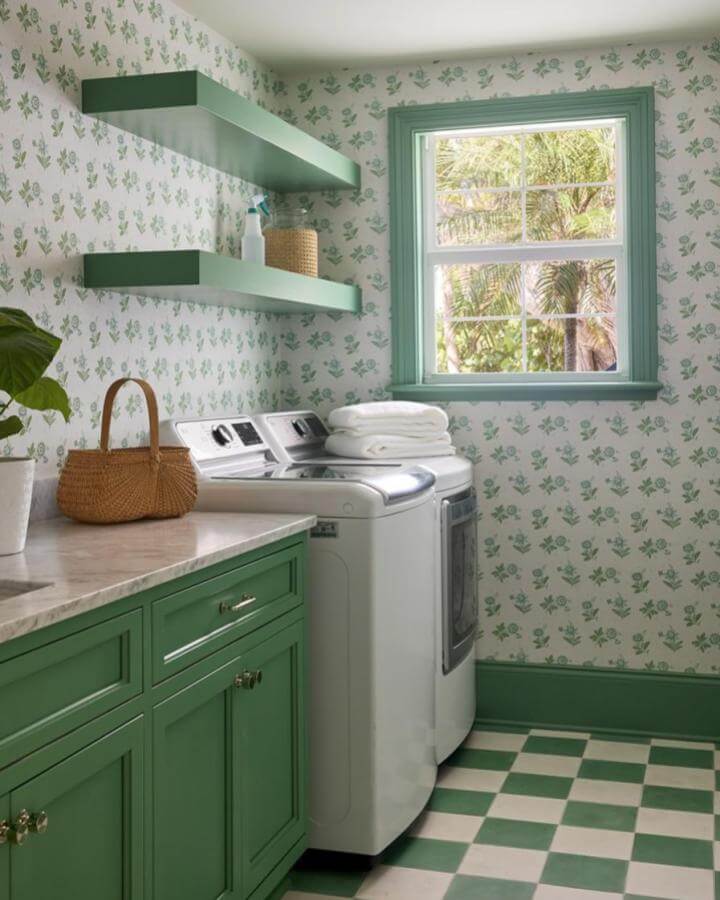 Green cabinets and floating shelves in a laundry room from @demimabry with leafy wallpaper and checkered floor tiles.