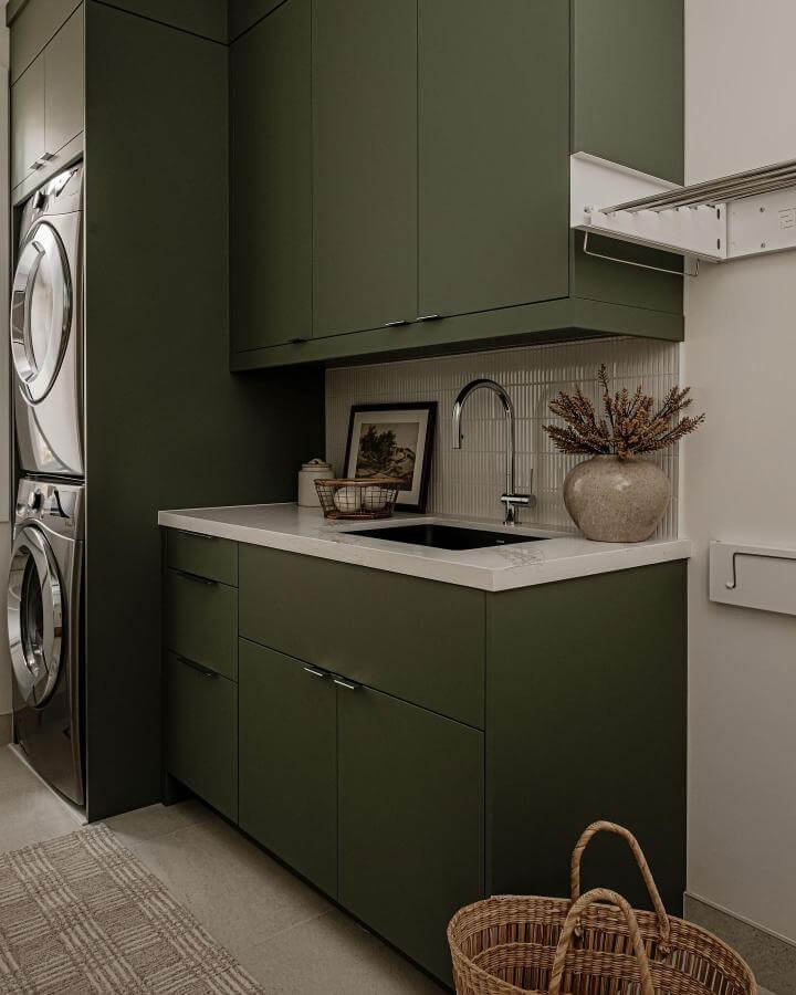 Deep sage green cabinetry in laundry room with white quartz countertop from @stefbrownphoto. Calm, modern green laundry room ideas with natural textures.