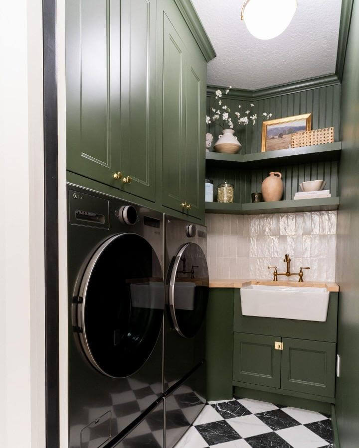 Deep green cabinetry laundry room with brass fixtures and checkered floor from @apartmenttherapy showcasing elegant green laundry room ideas.