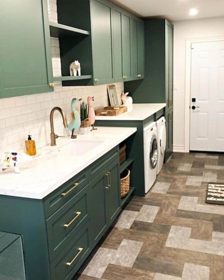 Matte green cabinets and white quartz countertops laundry room from @hartley_built with brass hardware and patterned floor.