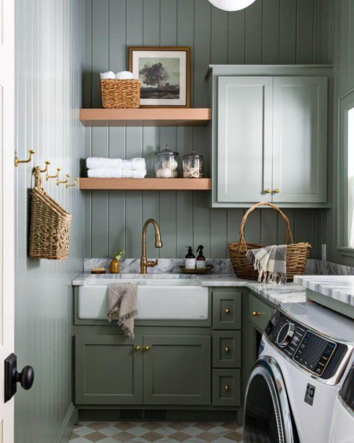 Green paneled cabinetry laundry room from @ashley_sullivan__. Brass accents and natural wood shelves complete this green laundry room ideas look.