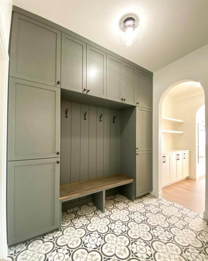 Olive green built-in mudroom cabinetry from @little.rock.builders with natural wood bench and patterned tile floor.