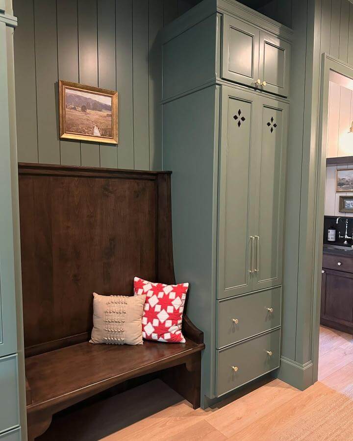 Dark wood bench and sage green cabinetry mudroom from @brickandbatter featuring cozy cushions and elegant detailing in green mudroom ideas.