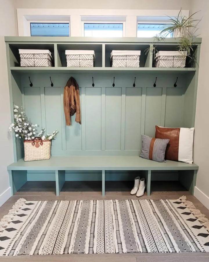 Muted sage green built-in bench and storage from @sweetvalleyacres with black hooks and patterned rug in cozy entry space.