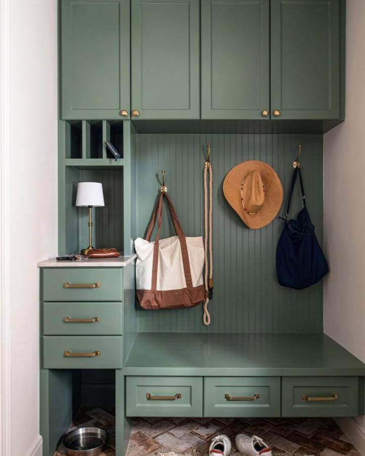 Green built-in mudroom with brass hardware from Ellen Renee Photography. Includes beadboard panels, marble countertop, and practical hanging hooks.
