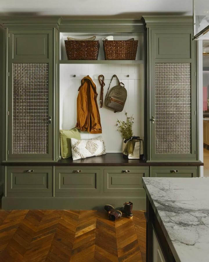 Olive green built-in mudroom bench with woven cane doors and dark wood countertop from @garruppo. Organized entryway with textured accents.