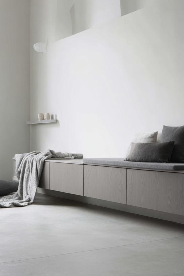 Floating white storage bench with grey cushions and minimalist wall-mounted shelf. Clean lines and neutral tones create seamless built-in seating.