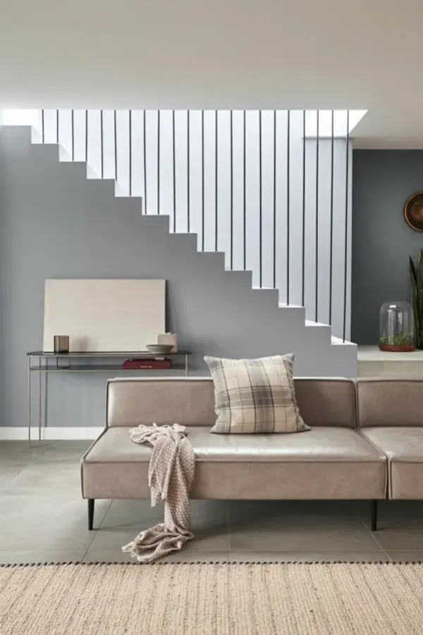 Modern beige sectional sofa beneath floating white staircase in contemporary minimalist living space