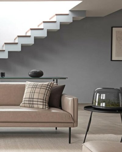 Contemporary floating staircase with wooden treads against charcoal wall. Features glass console table and neutral sofa beneath.
