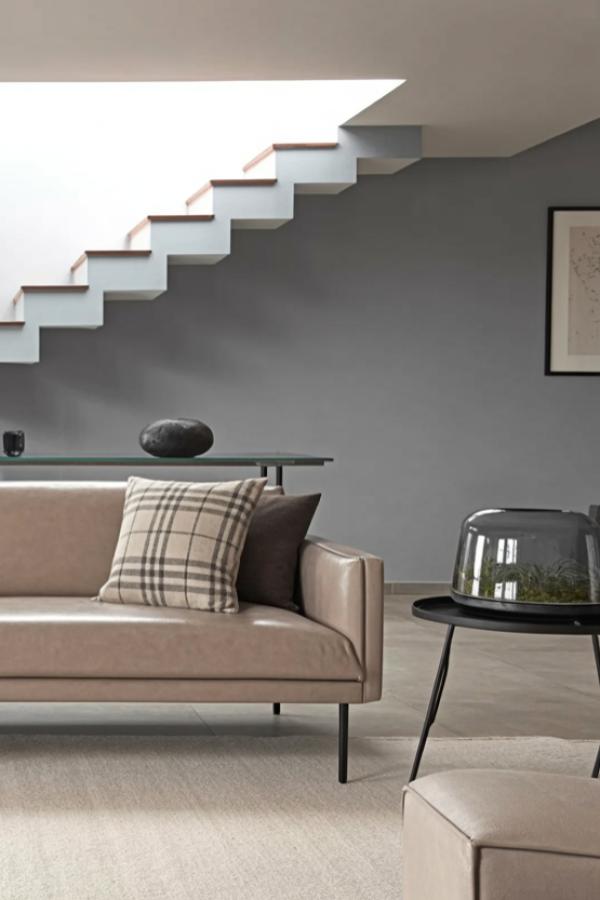 Contemporary floating staircase with wooden treads against charcoal wall. Features glass console table and neutral sofa beneath.