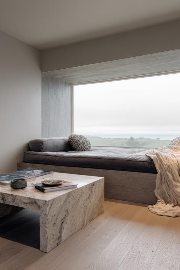 Modern built-in window seat with marble coffee table and neutral tones in contemporary living space.