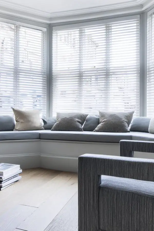 Modern built-in window seating area with grey cushions and white blinds in contemporary home interior.