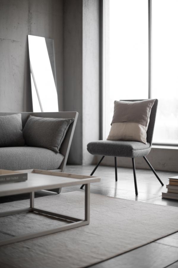Modern grey sofa and chair setup against concrete walls. Clean minimalist furniture arrangement with natural lighting.