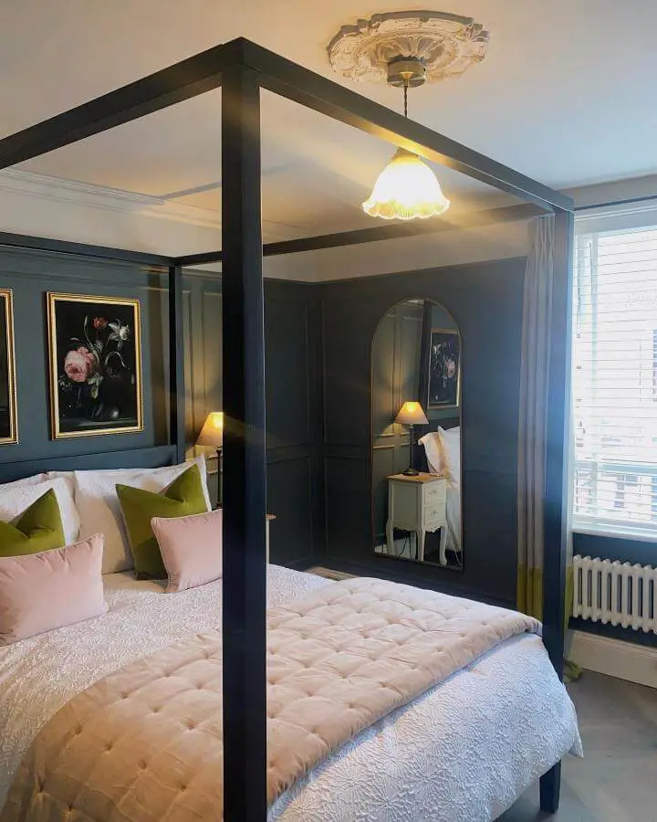 Navy bedroom with four-poster bed from @theoldvillagepostoffice. Dark walls and colorful accent pillows create cozy atmosphere.