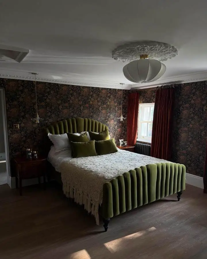 Fluted olive green velvet bed frame from @lydiabrightshome. Dark floral wallpaper and burgundy curtains complete the sophisticated look.