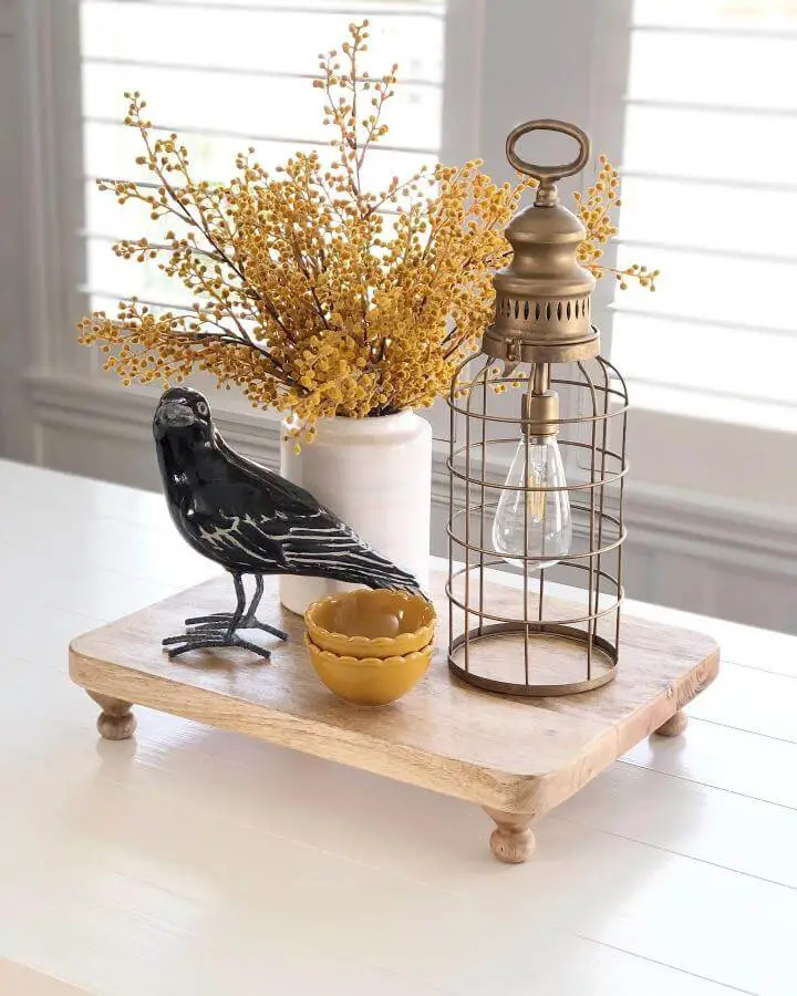 Rustic wooden tray centerpiece from @sweetroseandwren featuring black raven, golden berries, and brass lantern for halloween centerpiece ideas.