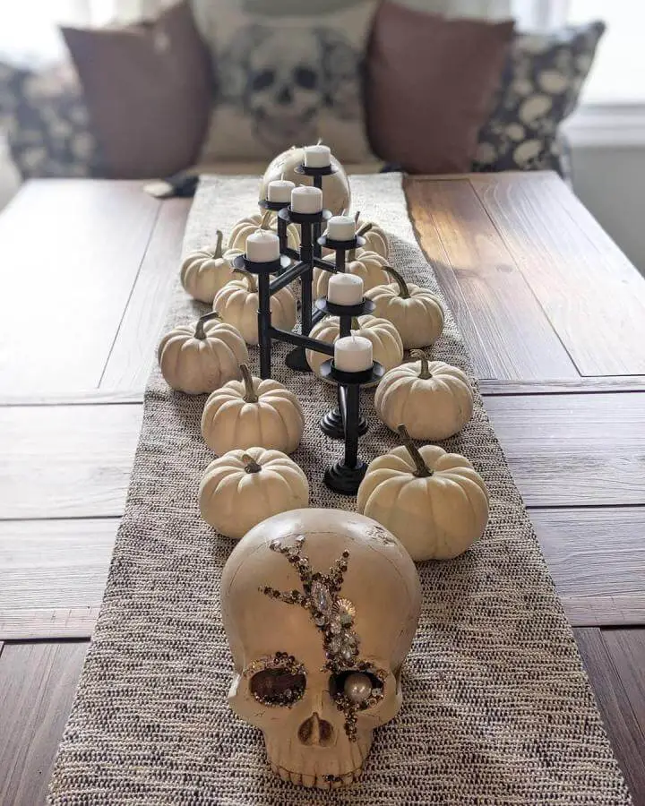 Cream pumpkin table display from @21figs featuring black metal candelabra and decorative skull on burlap runner.