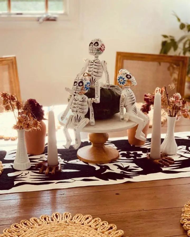 White skeleton figurines on wooden stand from @peruvianalifestyle. Surrounded by cream candles and dried autumn flowers.