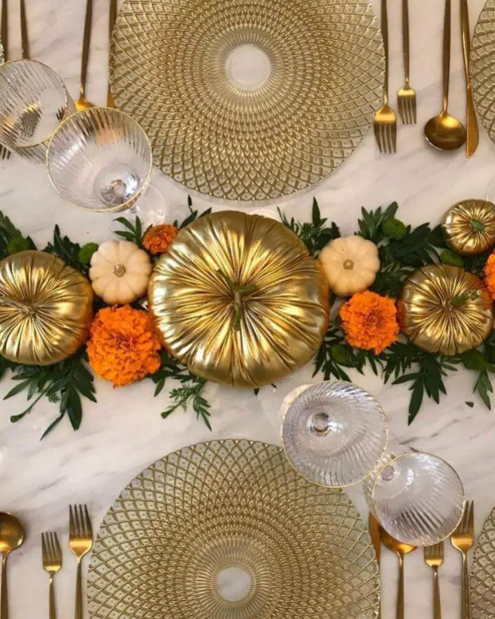 Elegant golden pumpkin table arrangement from @mayflowerdubai featuring metallic gourds, orange marigolds and green foliage.
