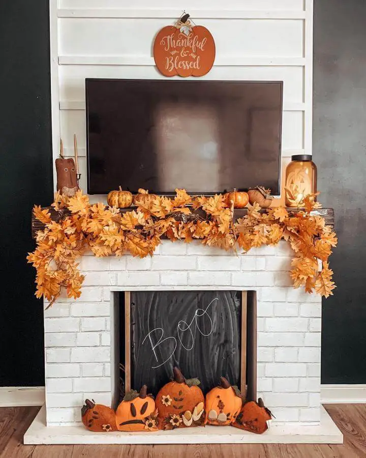 Orange autumn leaf garland mantel from @mariaellenk. White brick fireplace with wooden pumpkins and mason jars.