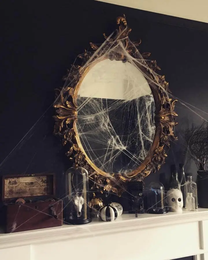 Ornate gold mirror from @renovating_elmfield draped with spider webs and spooky mantel accessories.