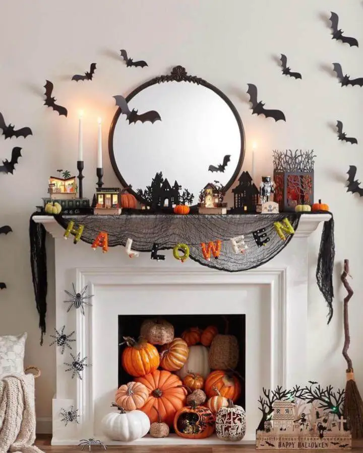 Black paper bat cutouts from @frameworkdigitalmedia swarming around decorated white fireplace mantel with orange pumpkins and Halloween village.