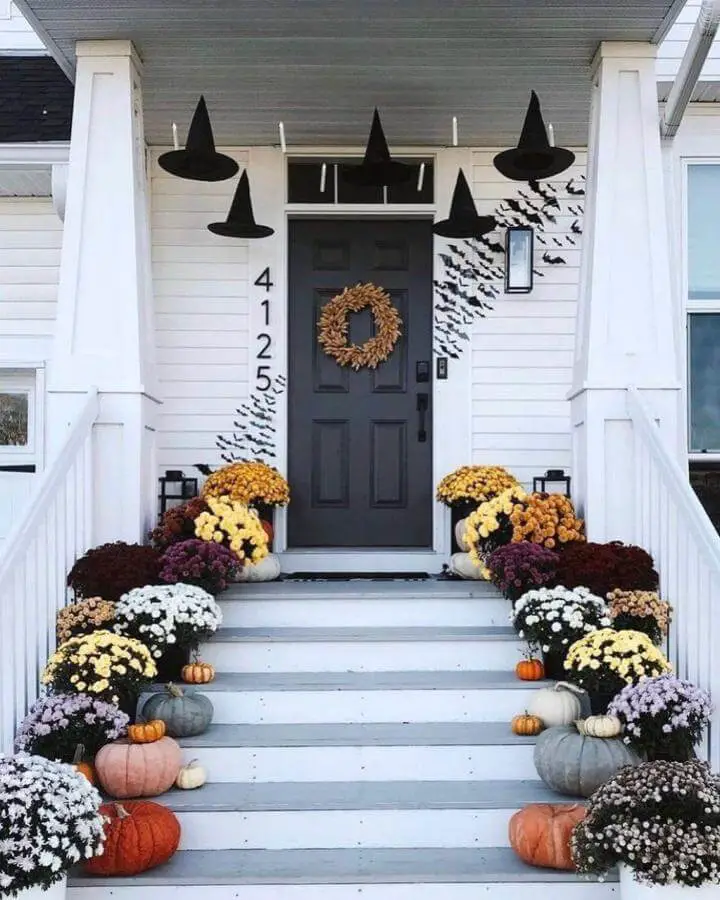 White farmhouse porch with suspended black witch hats and autumn mums for halloween porch decor from @3acrelife.