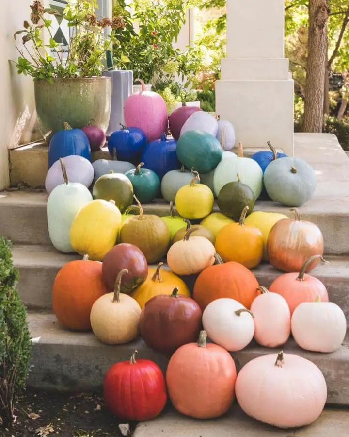 Colorful painted pumpkins arranged on porch steps from @houselarsbuilt showing rainbow ombre effect.