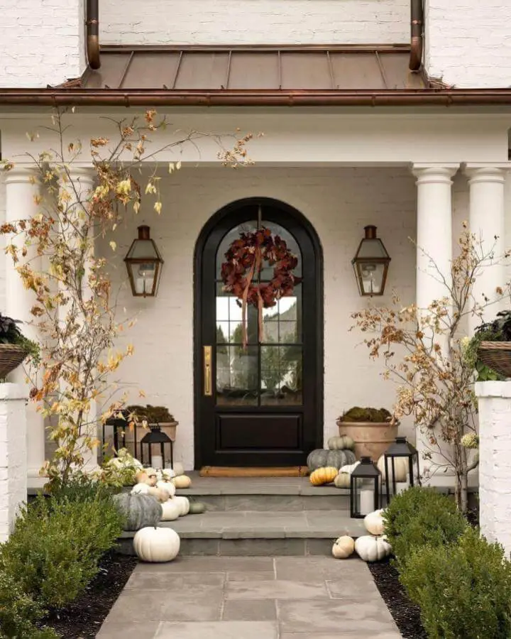 Elegant autumn front door from @cathyhaneyteam featuring burgundy wreath, white pumpkins, and copper lanterns on stone steps.