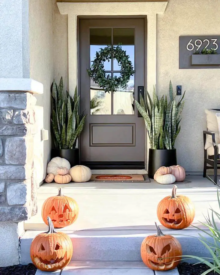 Neutral porch entry from @50_shades_of_neutral with carved orange pumpkins arranged on concrete steps and planters.
