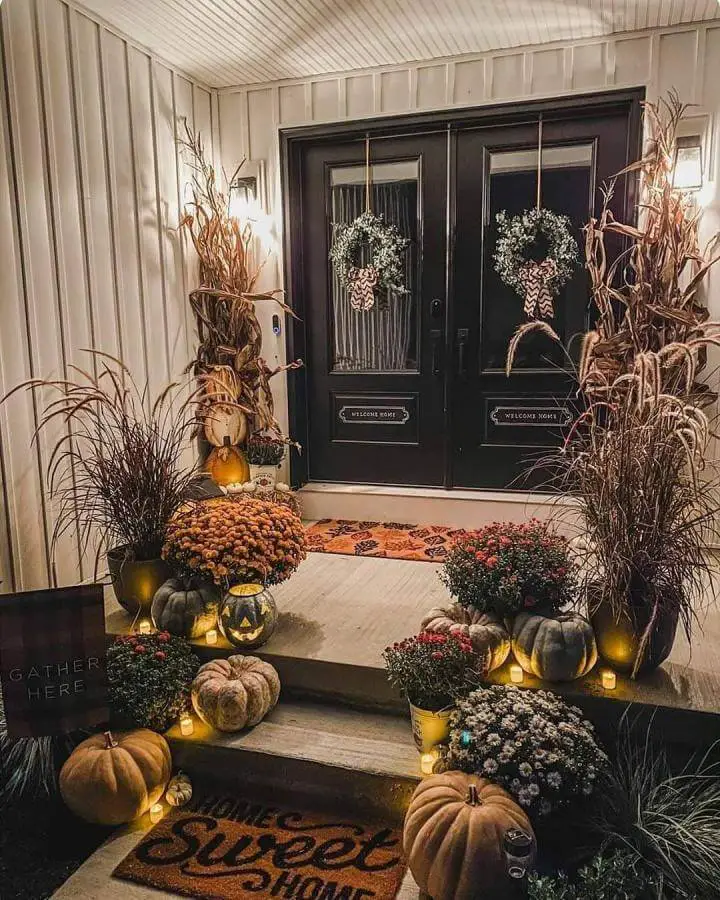 Autumn entrance with string lights and halloween porch decor from @lifeisaboutthebermonts. Pumpkins and mums arranged on steps.