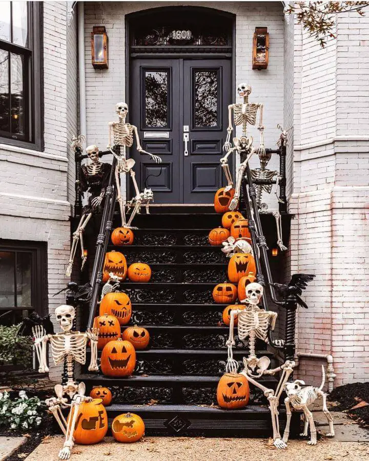 Elaborate skeleton display on black steps from @modernglamhome. Multiple skeletons positioned with carved orange pumpkins creating spooky entrance.