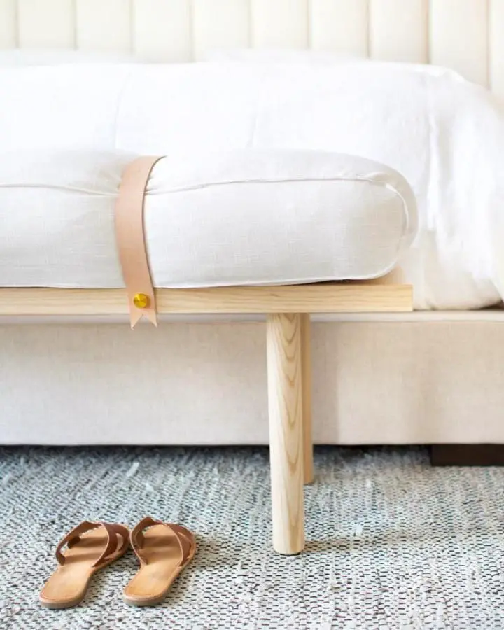 Minimalist wooden bench from @kristimurphydiy. Features tan leather strap detail and white bedding backdrop.