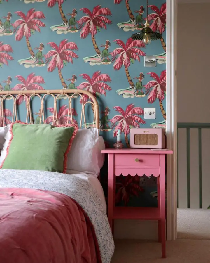 Bright pink painted bedside table from @megmonde featuring tropical wallpaper and vintage radio styling.