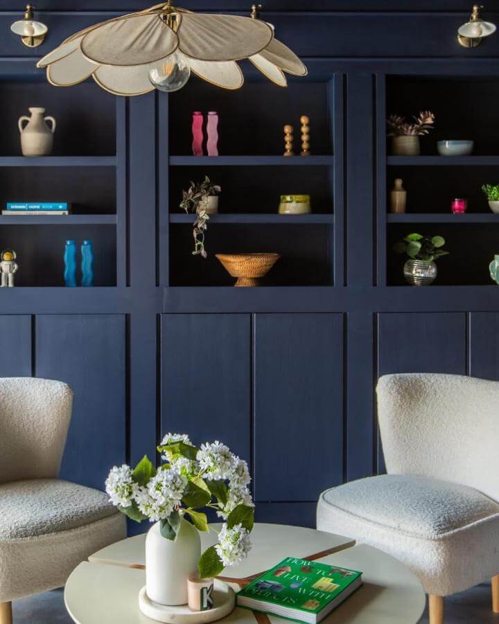 blue painted Ikea Billy bookcase transformation in living room with cream chairs and floral centerpiece from @our_bears_home rich navy storage background