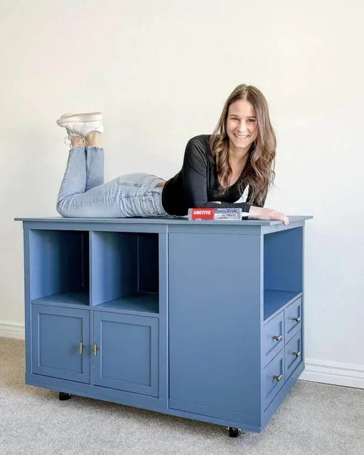 Blue painted multifunctional craft table with storage compartments and brass handles from Designing Parkside. Woman lying on table smiling.