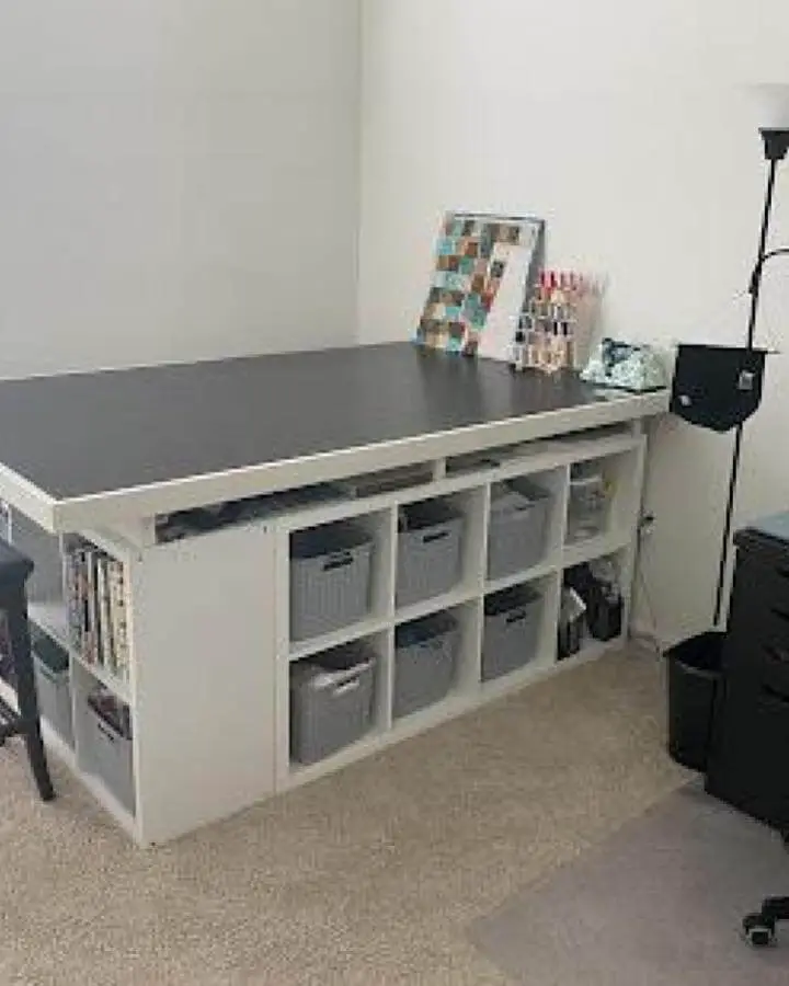 Gray bin-filled white cubby storage with black tabletop in craft room from @mwoerner. Organized ikea craft table hacks with a clean, functional design.