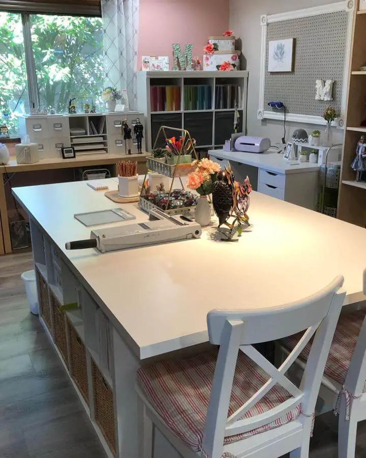 white craft table island with woven baskets and cushioned chairs in craft room from Anchored Strengthened Love organized ikea craft table hacks with tidy storage and workspace