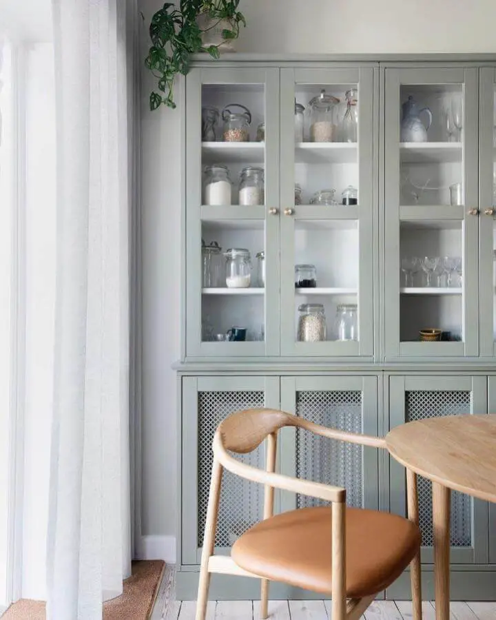 Sage green cabinet with perforated metal panels from @unikkerum. Glass-front storage above wooden dining chair.