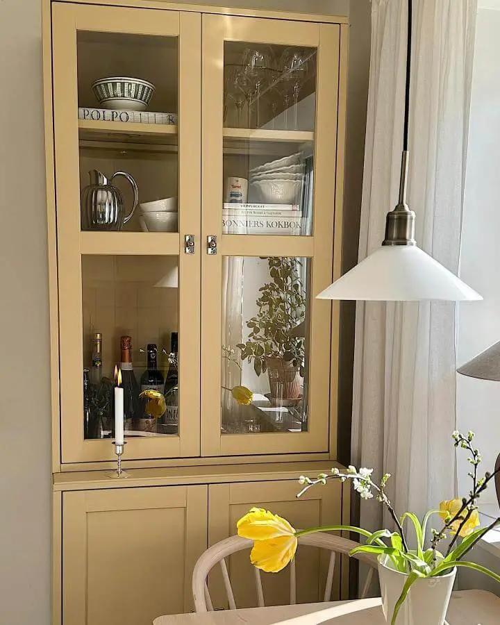 Beige glass-door cabinet from @carolinashome with styled glassware and decor in dining space.