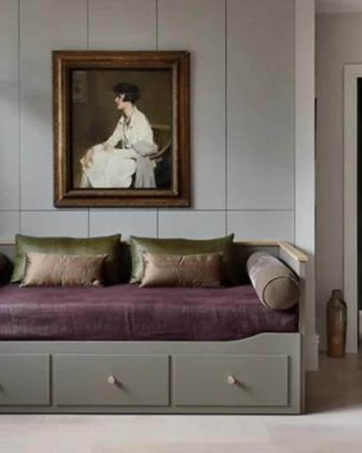 Muted green Ikea Hemnes daybed with plum velvet bedding from Robinson Van Noort. Elegant storage and cozy cushions with vintage art.