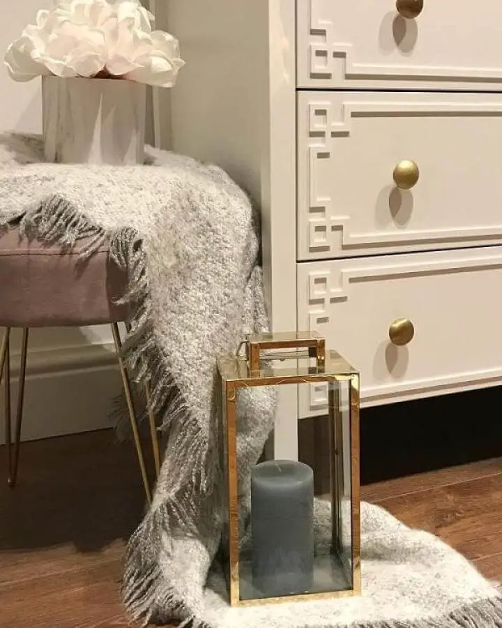 White dresser with Greek key edge trim and brass knobs styled with cozy throw and glass lantern from @marbleandmoree ikea koppang hacks.