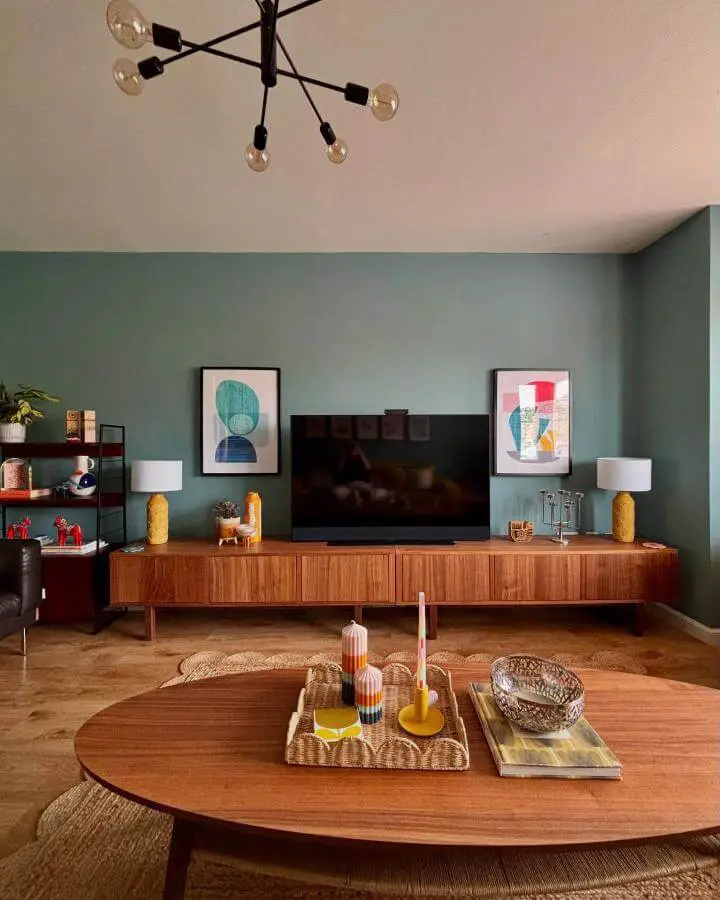 Walnut wood media console in living room with green walls and colorful decor from @fromcity2suburb showcasing ikea media center hacks & ideas.