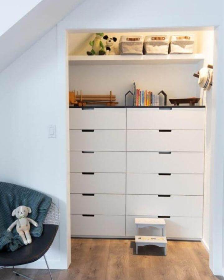 White minimalist built-in dresser from Lindi and Russ featuring ikea nordli hacks tucked neatly under a slanted ceiling with wood flooring and a cozy chair nearby.