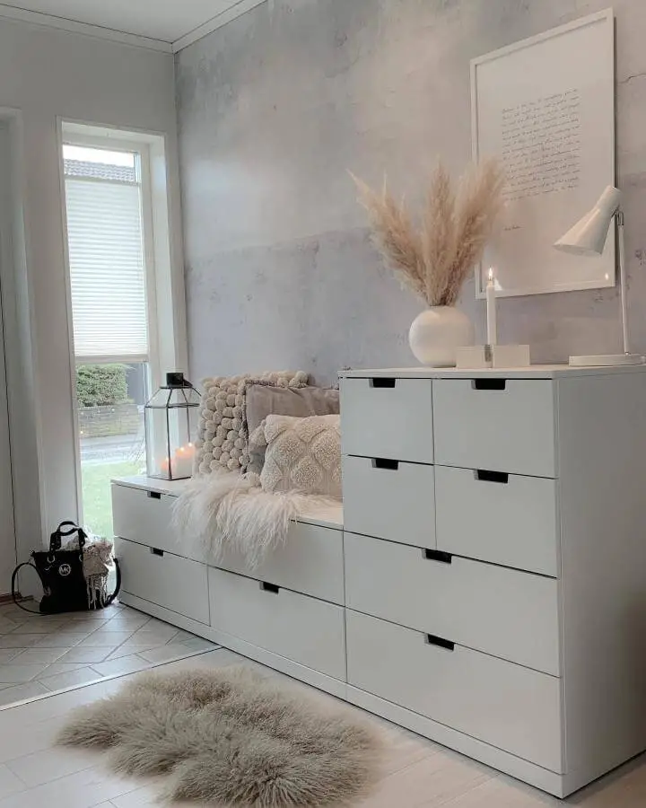 White minimalist ikea nordli hacks storage bench with soft beige pillows and pampas grass from @mykindoflike. Cozy and stylish small space idea.