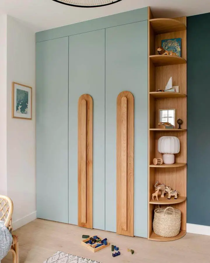 Soft green wardrobe with bold wooden handles and oak curved shelves from @plum.living. Ikea pax hacks with playful storage design.